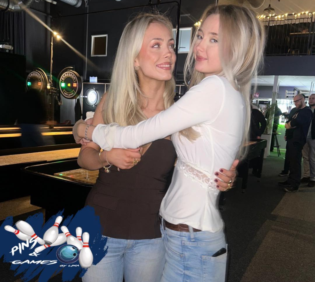 TvÃ¥ leende kvinnor kramar varandra i en avslappnad miljÃ¶ med bowlingbanor i bakgrunden.